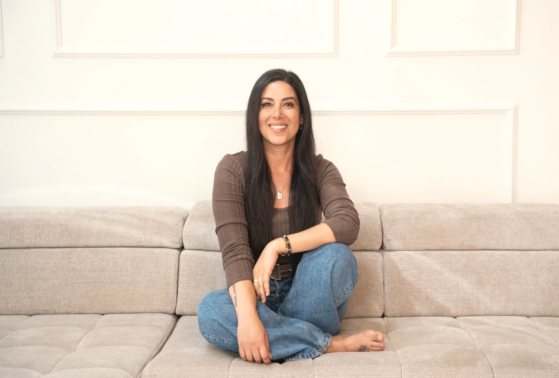 Anna Gala, meditation teacher and author of My Morning Magic Journal, smiling while sitting cross-legged on a beige sofa